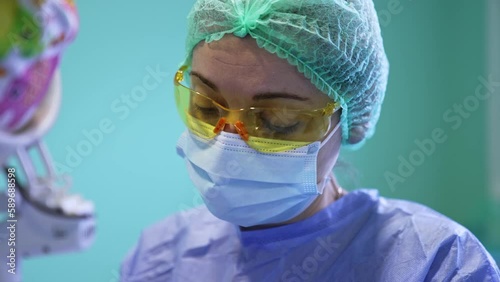 Assisting doctor in yellow goggles, mask and cap. Close up portrait of a medic during surgery. photo