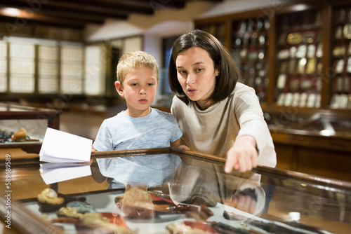 Young female tutor with boy looking at exposition in glass case in historical museum