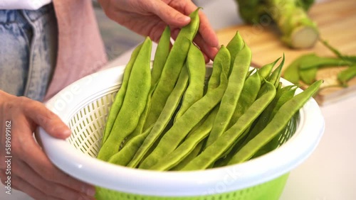 A woman in kitchen at home holding a salad spinner with helda romano beans and checks fresh vegetables by touching them with his hands. The concept of a healthy nutrition, green vegetables for detox photo