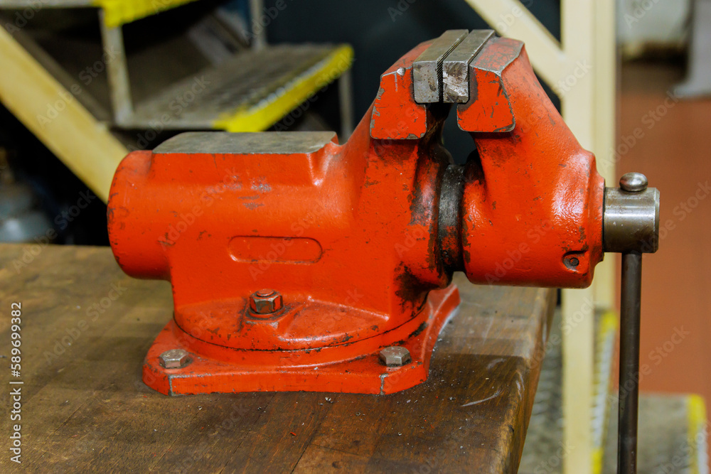 The vise is fixed on the metalworking workbench. A red vise on a wooden workbench at a metalworking plant. Bench tools.