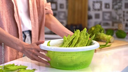 A girl in a pink shirt tossing up Green vegetables in salad spinner stands in the kitchen at home and is going to cook a vegetarian diet salad. Healthy eating and Home cooking food concept. photo