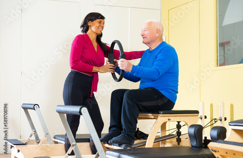 Professional trainer helps an elderly man restore health with gymnastic ring in a pilates class