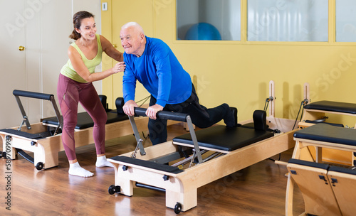 Elderly man doing exercise with her personal trainer in pilates studio © JackF