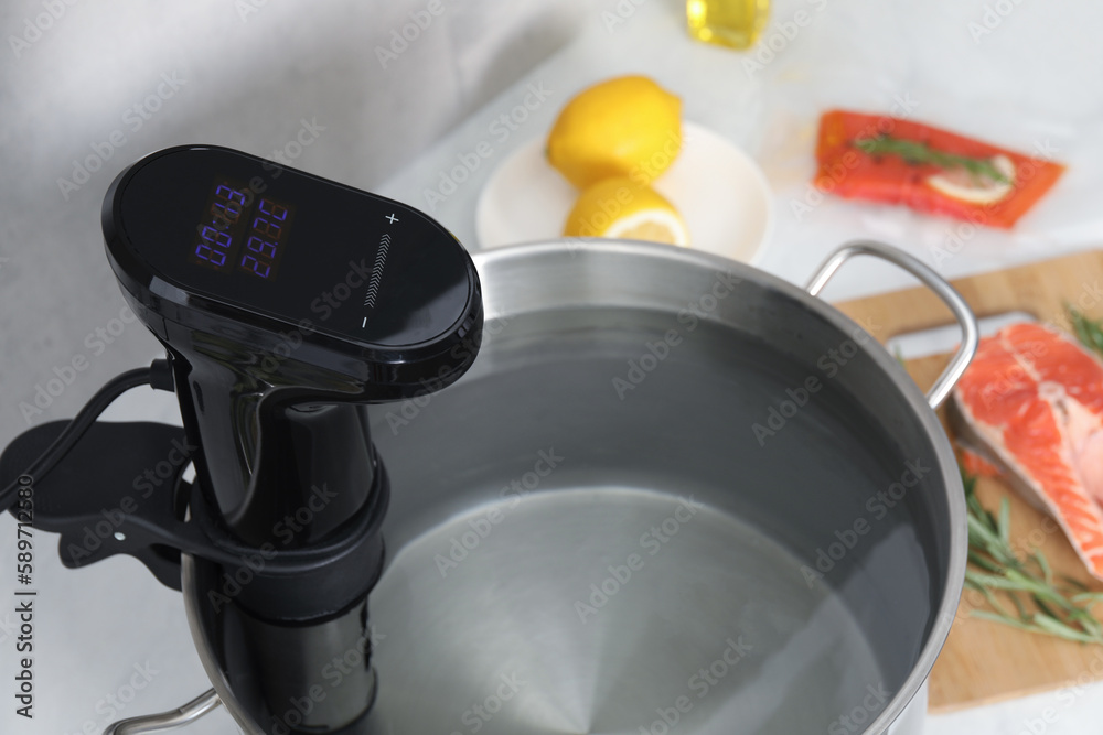 Sous vide cooker in pot on white table, closeup. Thermal immersion circulator Sous vide cooker in pot on white table, closeup. Thermal immersion circulator