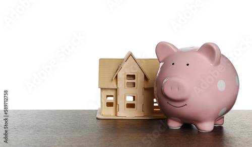 Piggy bank and house model on wooden table against white background. Saving money concept
