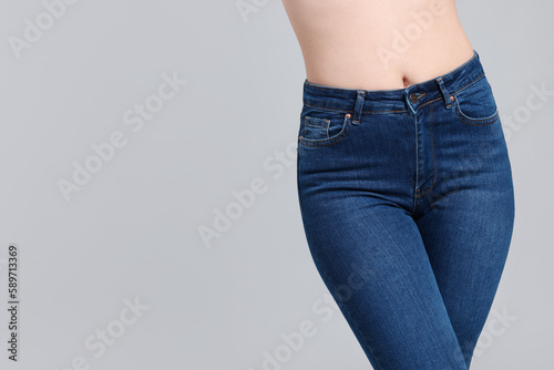 Woman in stylish jeans on grey background, closeup. Space for text