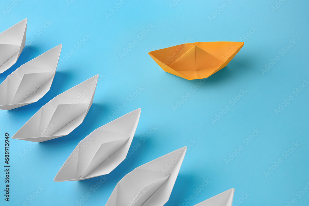 Yellow paper boat floating away from others on light blue background. Uniqueness concept Yellow paper boat floating away from others on light blue background. Uniqueness concept