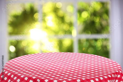 Red and white checkered tablecloth on table near window. Space for text