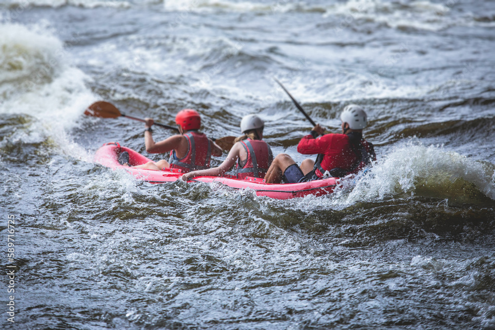 Raft boat during whitewater rafting extreme water sports on water rapids, kayaking and canoeing on the river, water sports team with a big splash of water, 3 persons in a raft boat