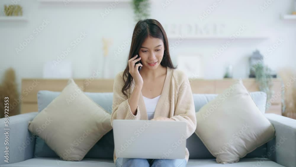 Young asian woman using computer laptop and mobile smartphone while seated on couch at home Young asian woman using computer laptop and mobile smartphone while seated on couch at home