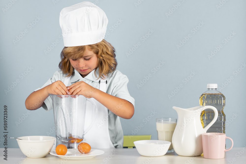 Portrait of a 7, 8 years old child in cook cap and apron making fruit salad and cooking food in kitchen. Cute little blonde happy smiling chef. Portrait of a 7, 8 years old child in cook cap and apron making fruit salad and cooking food in kitchen. Cute little blonde happy smiling chef.