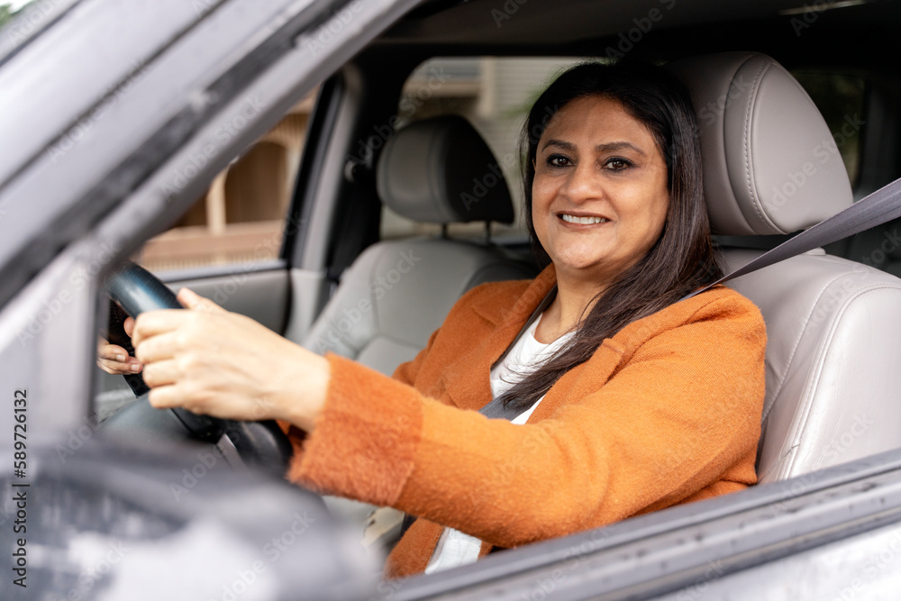 Portrait of smiling mature Indian woman driving a new car. Transportation, road trip, car sharing concept