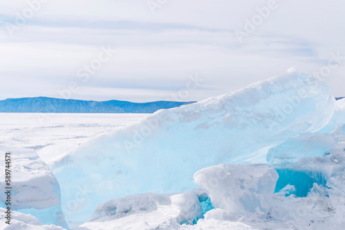 Winter landscape with ice hummocks sparkling in the sun and mountains of Baikal in Siberia at sunset.