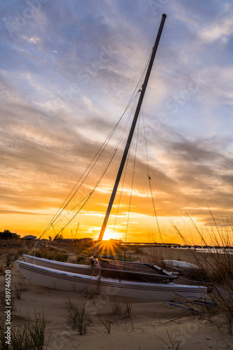 A Catamaran Sitting on the Beach As the Sun Sets in the Center of the Mast in Norfolk Virginia Ocean View © Kyle
