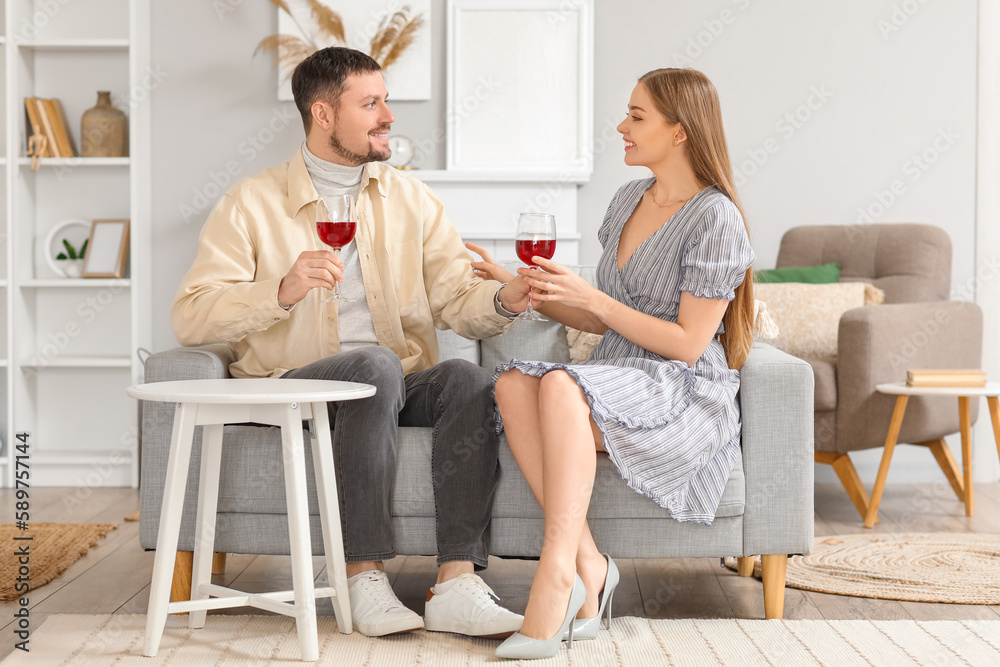 Fototapeta premium Young couple with glasses of wine sitting on sofa at home