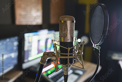 Microphone Close-up in Recording Studio - A close-up of a microphone with a blurred background of a professional recording studio, featuring mixer and monitor equipment.