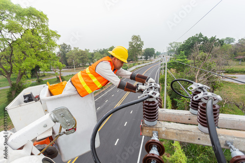 Asian electrician with crane truck is installing cable lines and electrical transmission on electric power pole against blue sky background