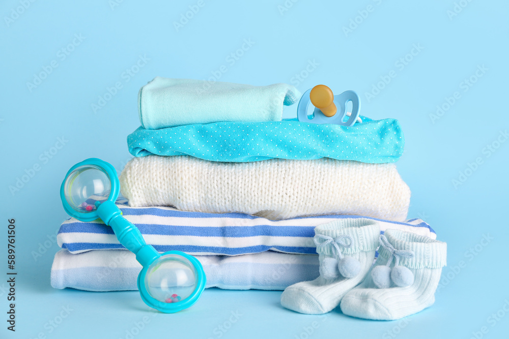 Fototapeta premium Stack of baby clothes, rattle and pacifier on color background