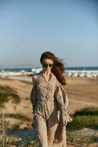 a woman in a beige dress stands on the sand at a resort in sunglasses enjoying the warm weather