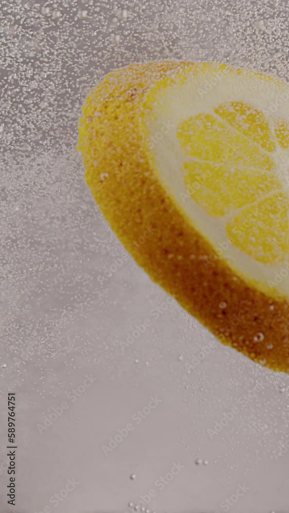 a slice of lemon falls into soda water, forming bubbles on a white background
