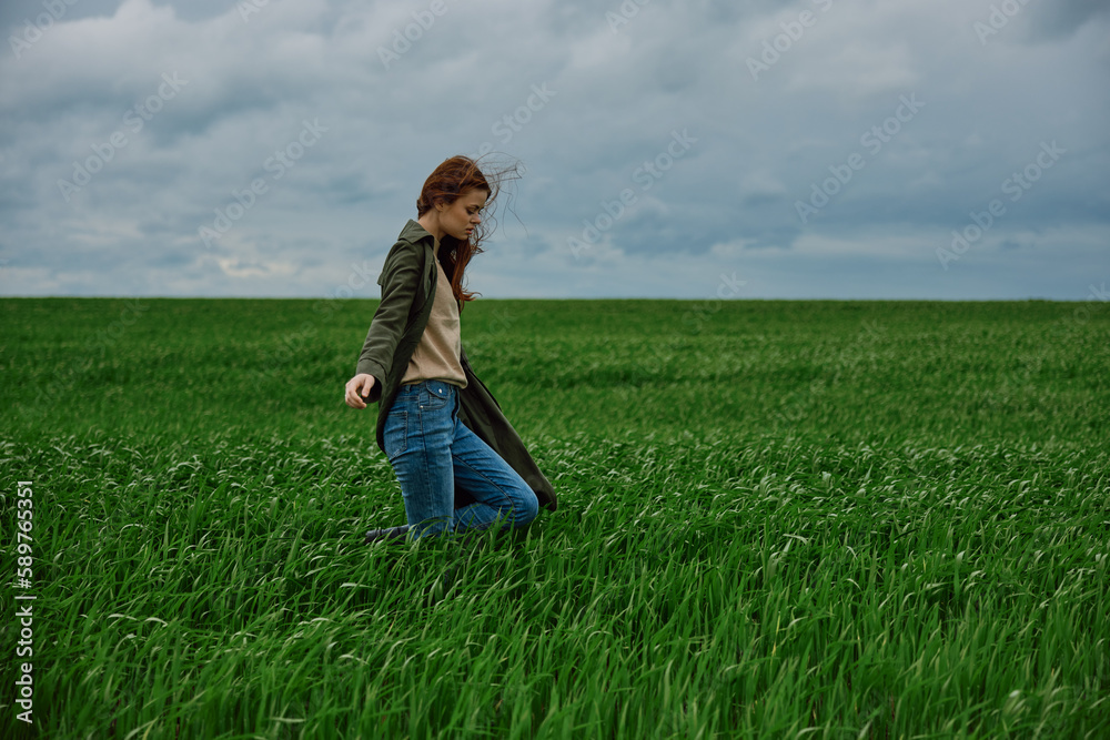awoman in a coat walks through a green field in rainy weather. Strong wind, harmony with nature awoman in a coat walks through a green field in rainy weather. Strong wind, harmony with nature