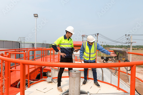 Two heavy industrial engineers standing in a standard water treatment plant use digital tablet computers and chatting. Asian industry professionals © somchai20162516