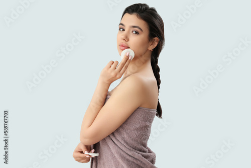 Young woman removing makeup with cotton pad on light background