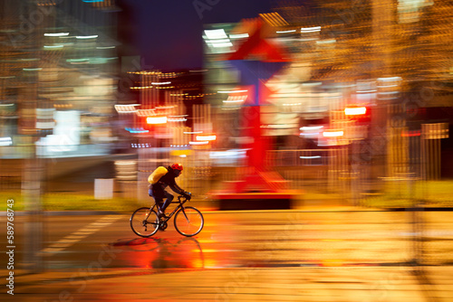Cyclist on wet road. Person on the slick way to work in the rain in the city at night. Panning shot. Germany, Stuttgart.
