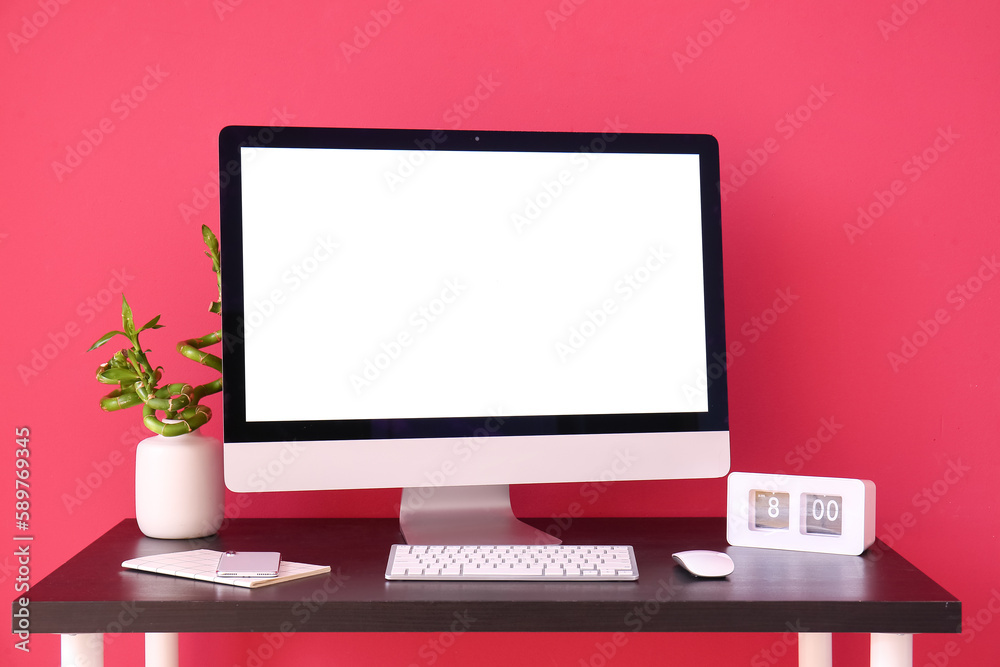 Workplace with computer, mobile phone and clock near red wall Workplace with computer, mobile phone and clock near red wall