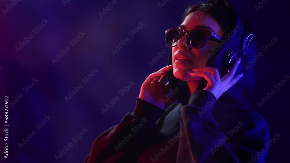 Hipster cyber female DJ listening music in headphones dancing ultraviolet neon backlit closeup