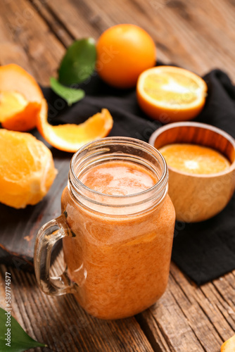 Glass of healthy smoothie and peeled orange on wooden table