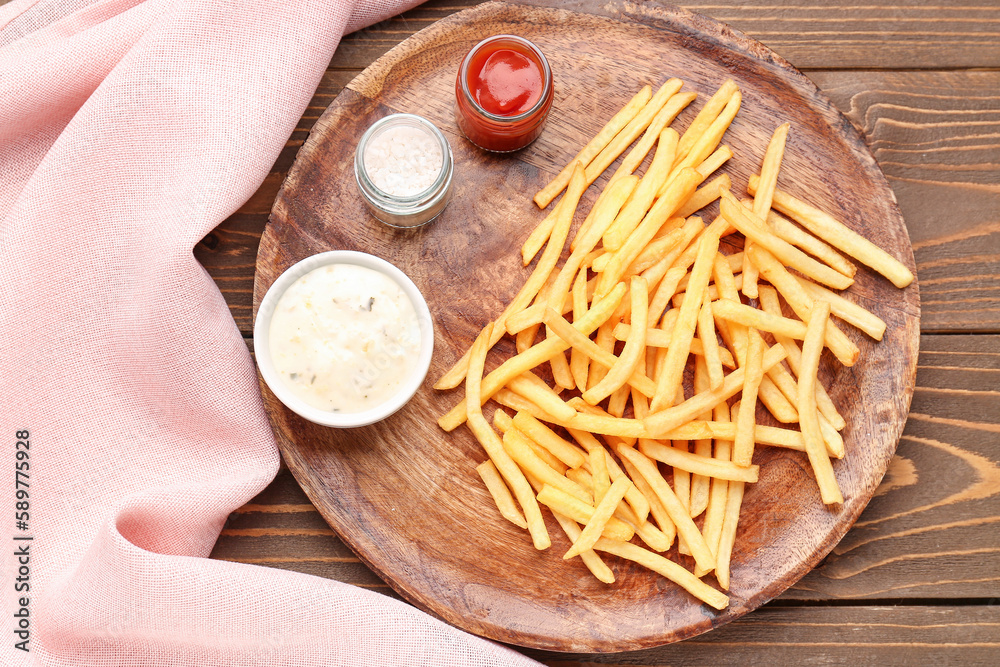 Tray with tasty french fries, sauces and salt on wooden background