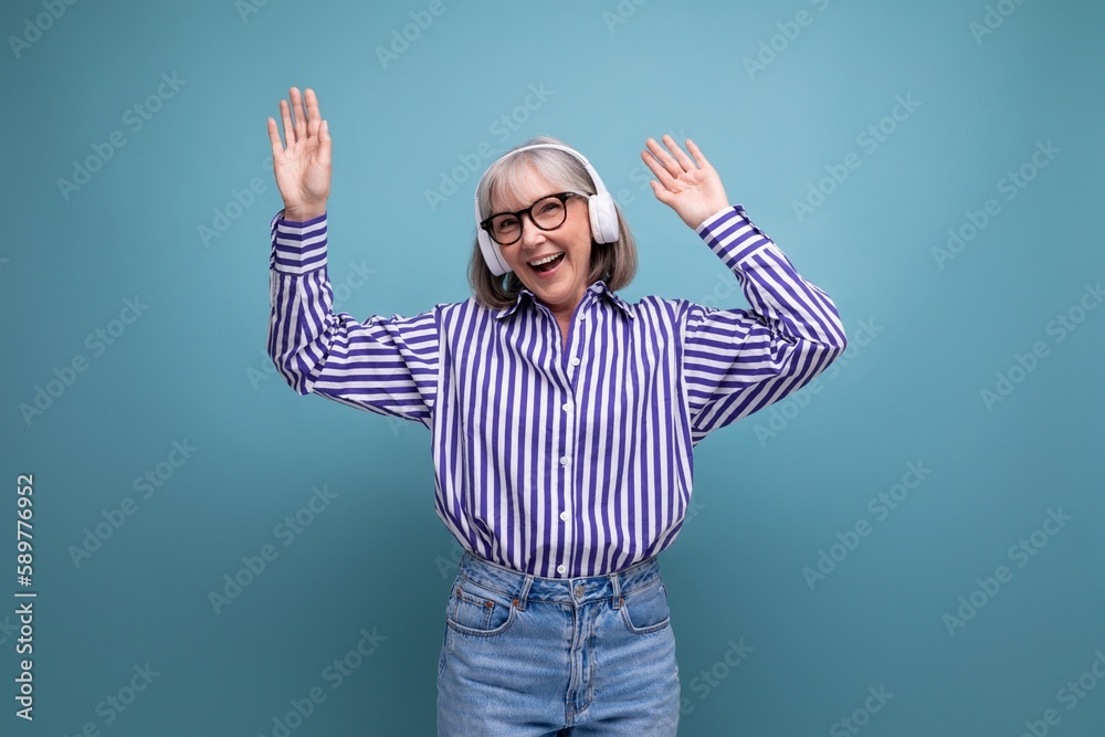 Naklejka premium happy middle aged woman with gray hair with headphones on bright studio background