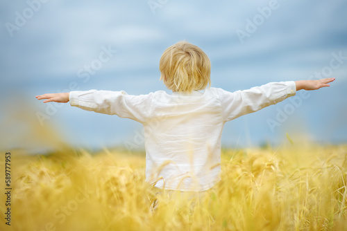 Pray for Ukraine. Child is on the background of bly sky and yellow wheat field. Background have colors of the Ukrainian flag. Concepts of peace and independence. photo