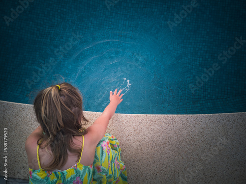 Obraz na płótnie A little girl checks the water condition before swimming in the pool. w salonie