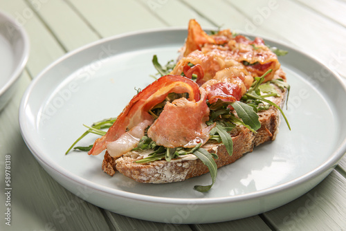 Tasty bacon bruschetta with arugula on green wooden background