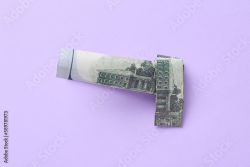 Origami gun made of dollar banknotes on lilac background
