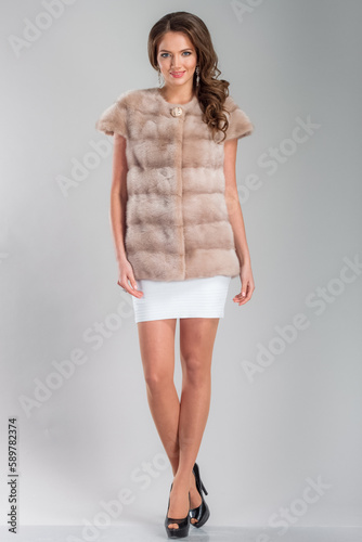 A beautiful young woman of European complexion wearing a fur coat, studio photoshoot