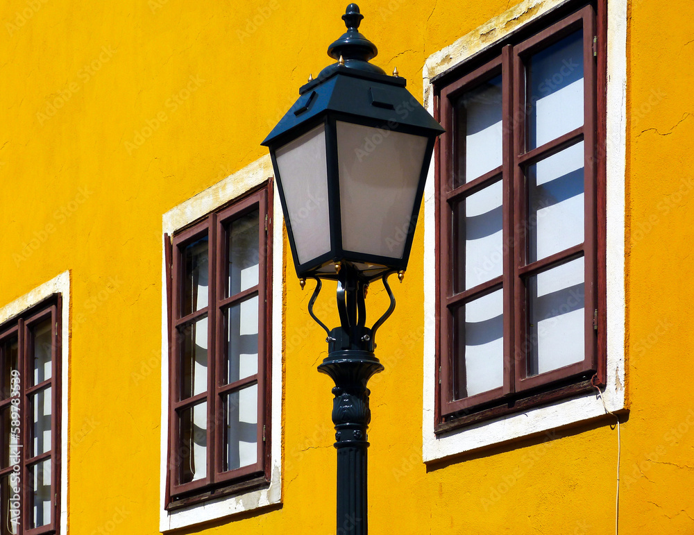 retro style street lantern. cast iron lamppost. colorful yellow stucco exterior wall background in old European town. old wood windows. urban street. travel, tourism concept. selective focus