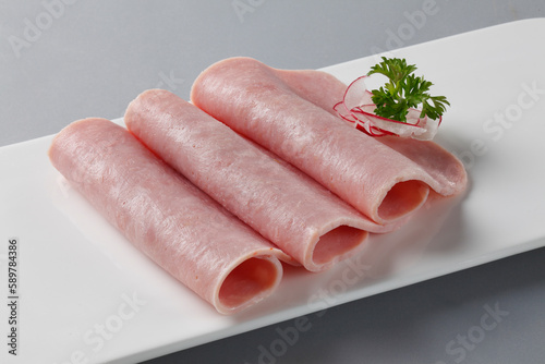 Photography Cooked ham slices on white plate on grey background.