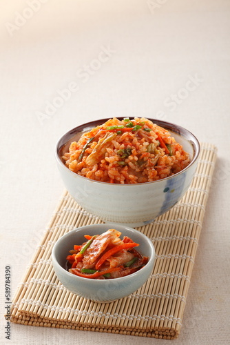 Kimchi stir fried rice, korean food in ceramic bowl and a small bowl of kimchi on bamboo place mat on white linen cloth background.