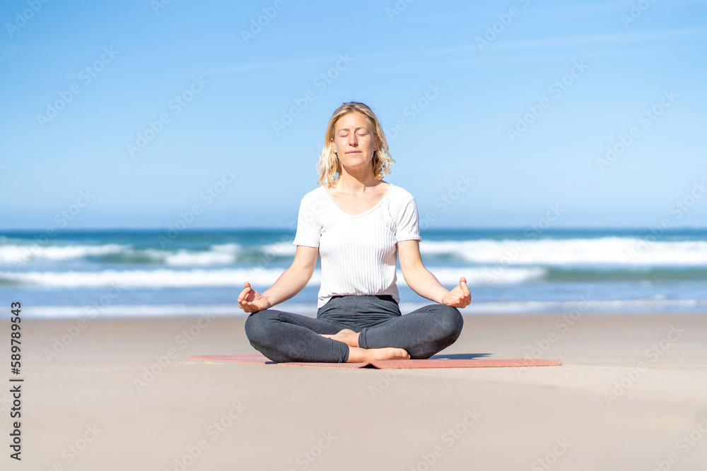 Yogi woman practicing yoga meditating, doing Ardha Padmasana exercise with eyes closed, Half Lotus pose with mudra gesture, working out outdoor. Well being, wellness concept