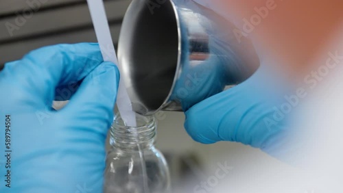 A chemical liquid is poured into a small flask by a scientist in a laboratory photo