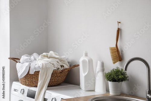 Basket with dirty clothes and detergent on washing machines in laundry room © Pixel-Shot