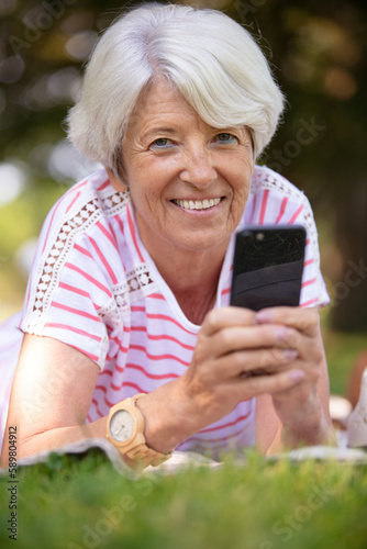 attractive senior woman sitting on the lawn with phone