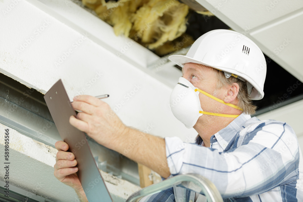male technician wearing mask looking at ceiling and taking notes male technician wearing mask looking at ceiling and taking notes