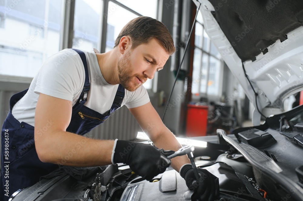 A mechanic is doing car checkup under the hood with flashlight at mechanic's shop. A mechanic is doing car checkup under the hood with flashlight at mechanic's shop.
