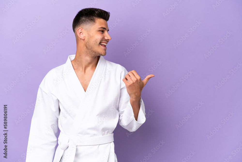 Young caucasian man doing karate isolated on purple background pointing to the side to present a product Young caucasian man doing karate isolated on purple background pointing to the side to present a product