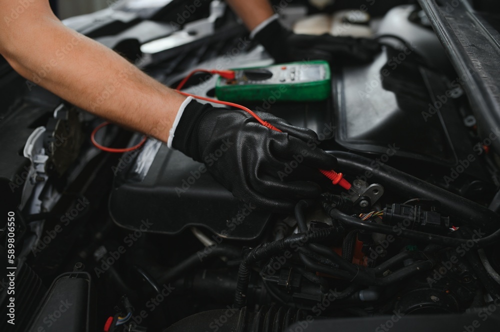 Car mechanic is using a multimeter with voltage range measurement to check the voltage level of the car battery.