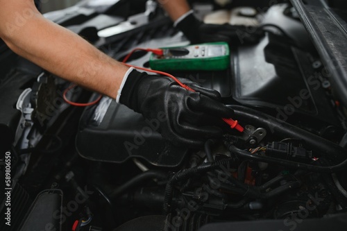 Car mechanic is using a multimeter with voltage range measurement to check the voltage level of the car battery.